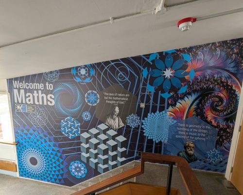 School hallway with a Welcome to Maths mural. Geometric patterns and math quotes decorate the wall.